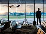 Business man standing in airport lounge looking through window bay at airplane taking off