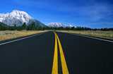 Freshly paved road set against pine trees and snow-topped mountains