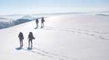 two couples of winter hikers with pack and skis passing over endless snowy hills on a cristal-clear sunny day