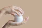 Hands holding and opening a white jar of cream