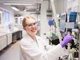 Female scientist in laboratory with lab coat, gloves and googles adjusting stiring equipment for a glass reactor