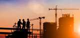 Construction site in morning light. Three workers in the foreground with construction cranes in the background.