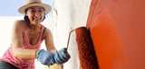 Smiling woman painting wall with red paint outdoors