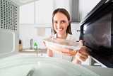 A woman placing a plastic container with food into the microwave