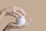 Hands holding and opening a white jar of cream