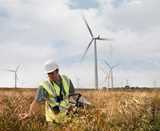 A man wearing a helmet standing in a field with grass, with windmills in the background