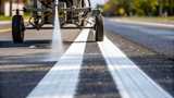 A detailed view of a paint sprayer releasing bright white line markings along a paved road