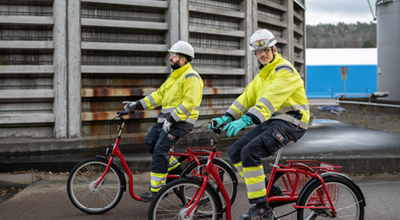 Two Nouryon employees in reflective outfits and wearing helmets riding red bicycles