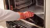 A hand with an orange glove wiping down the interior of an oven