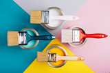 Blue, orange, pink, and off-white paint cans with brushes of similar colors